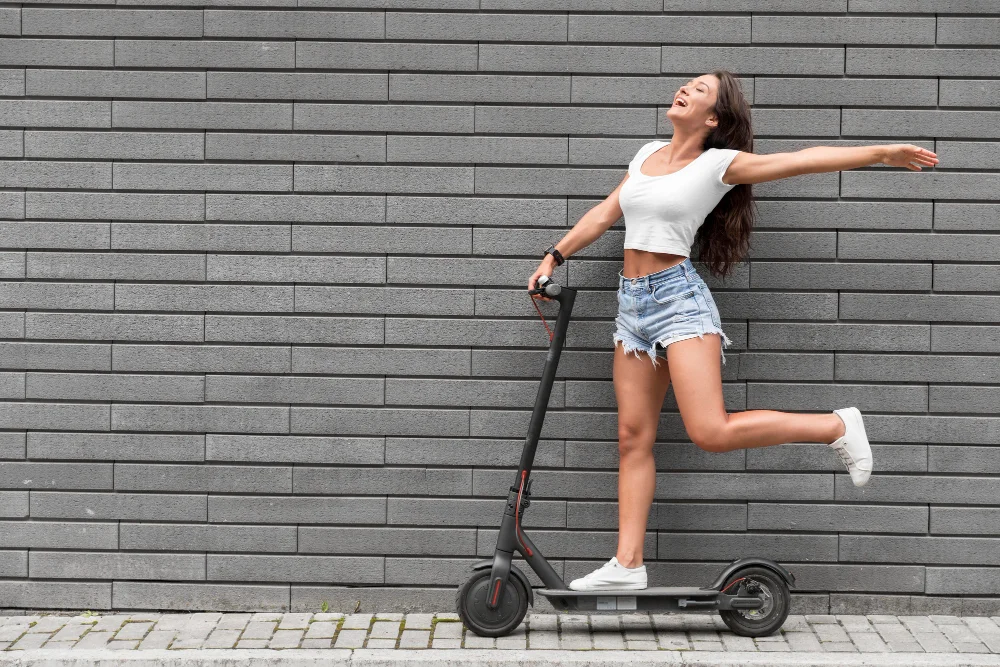 Una mujer posa felizmente parada en una pierna sobre un monopatín eléctrico